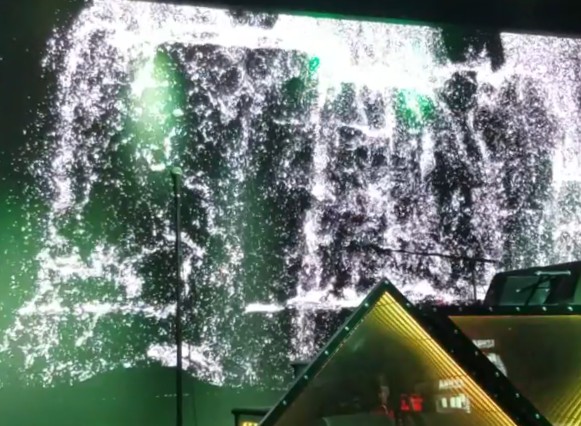 A white particle waterfall simulation cascading across the Planet 13 entry LED wall, lit green above a stage